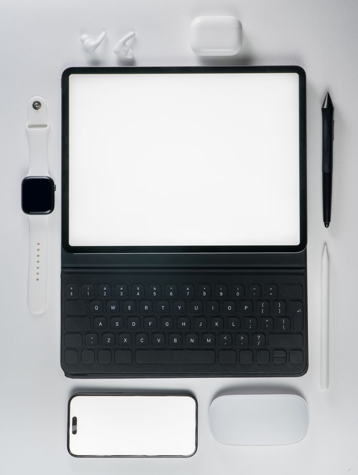 A flat lay of modern tech gadgets featuring a tablet, smartphone, and accessories on a white background.